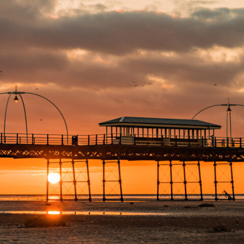 Birds fly over Southport Pier as the sun sets