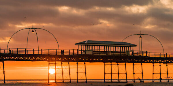 Birds fly over Southport Pier as the sun sets